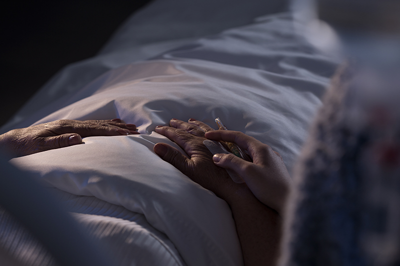 older person in bed - view of hands and bedding.