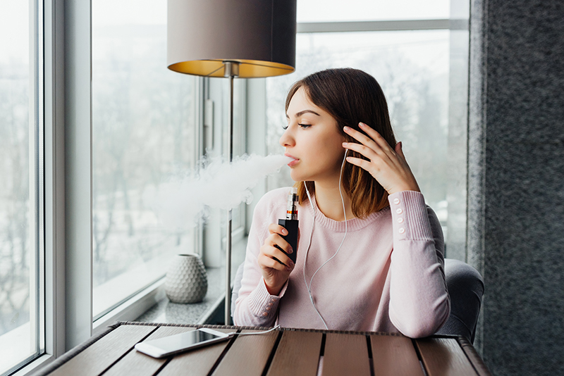 Female looking out window smoking vape