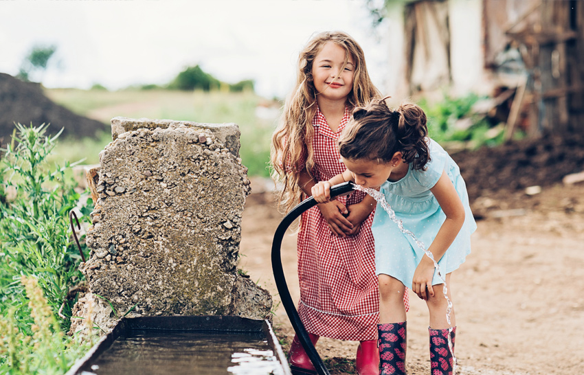 two little girls drinking water from a hose