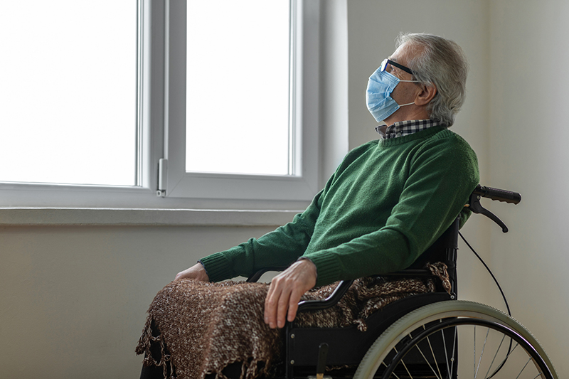 senior man in wheelchair with mask looking out window