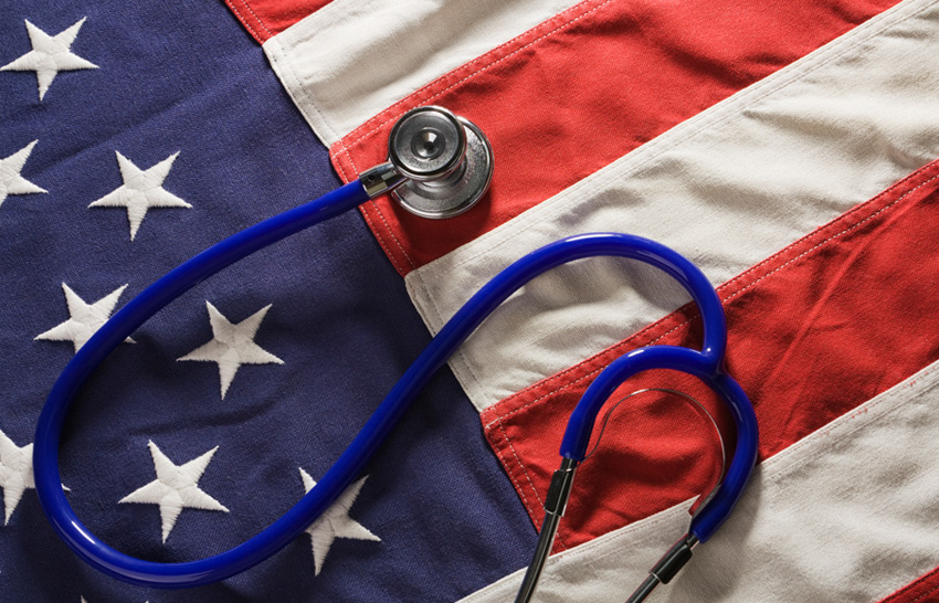 A stethoscope medical instrument resting on American flag fabric of red, white, and blue stars and stripes, representing concepts of healthcare and medicine reform, USA political changes affecting medical costs and health insurance benefit social issues, and ideas of listening, checking for healthy vital signs.