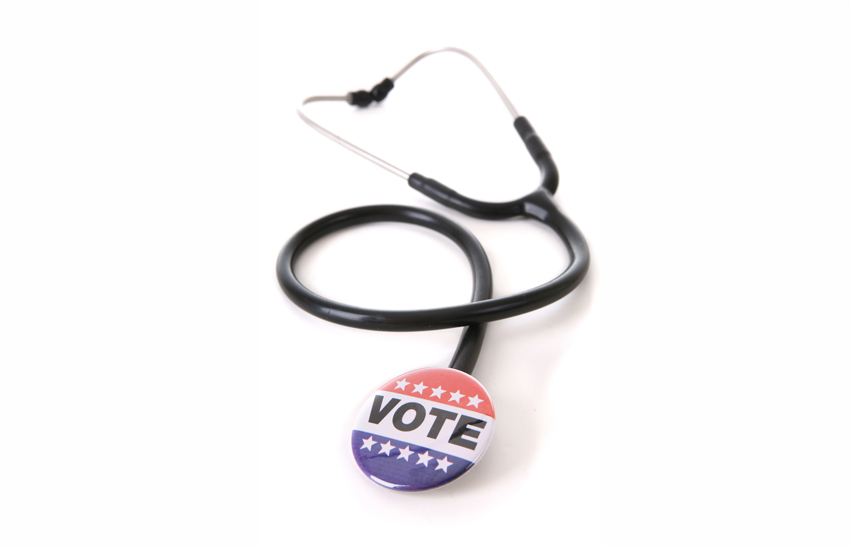 A stethoscope coiled on a white background, with a red, white, and blue ‘VOTE’ button at the end of the tubing in place of the chestpiece