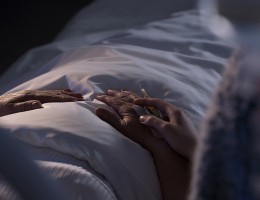 older person in bed - view of hands and bedding.