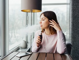 Female looking out window smoking vape