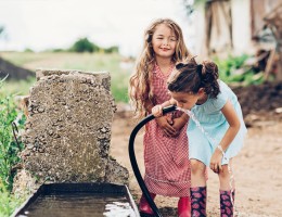 two little girls drinking water from a hose