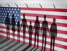 shadow of people against a wall with American flag and barbed wire.