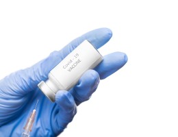 Gloved hands of contemporary virologist holding vaccine against covid19