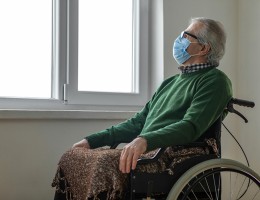 senior man in wheelchair with mask looking out window