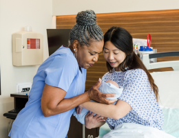 Senior female nurse carefully takes newborn from mid adult mother